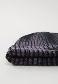 Strikbeanie med skiftende sorte og lilla striber, foldet ved kanten, med et tekstureret mønster og blødt stof.