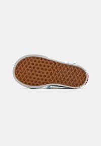 Såle av en sneakers med en teksturert brun gummioverflate med et diamantmønster, omgitt av en hvit mellomsåle og en liten rød detalj.