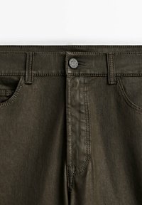 Taille de jean vert olive foncé avec fermeture par bouton métallique, passants de ceinture et poches avant cousues.