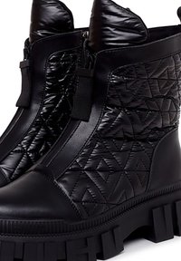 Botines negros acolchados con parte superior de textil brillante, suela de goma prominente, doble cremallera y patrones geométricos en los lados.