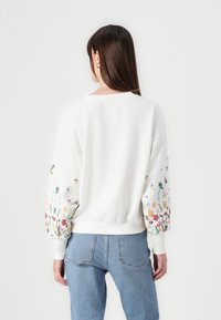 Sudadera blanca con bordados florales coloridos en las mangas, puños y dobladillo acanalados. Corte casual con cuello redondo.