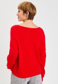 Pull rouge surdimensionné avec un large col, des manches longues et une texture douce. Associé à un jean en denim gris clair.