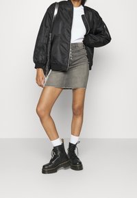 Chaqueta bomber de satén negra, camiseta blanca, falda de mezclilla gris con botones delanteros, botas negras con cordones y suela gruesa, y calcetines blancos hasta la caña.