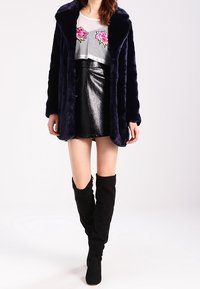 Abrigo de piel sintética azul marino, falda mini de charol negra, blusa de malla transparente con bordado de rosas rosas y botas de ante negras hasta la rodilla.