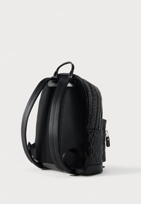 Μαύρο υφασμάτινο σακίδιο με επενδεδυμένους ιμάντες ώμων, πάνω λαβή και ανάγλυφο μοτίβο με το λογότυπο MK, εμφανιζόμενο από πίσω και πλάγια σε λευκό φόντο.