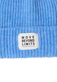 Jasnoniebieska dzianinowa czapka z prążkowaną fakturą i prostokątną białą metką z czarnym napisem "MOVE BEYOND LIMITS" oraz "FREEDOM STARTS HERE".