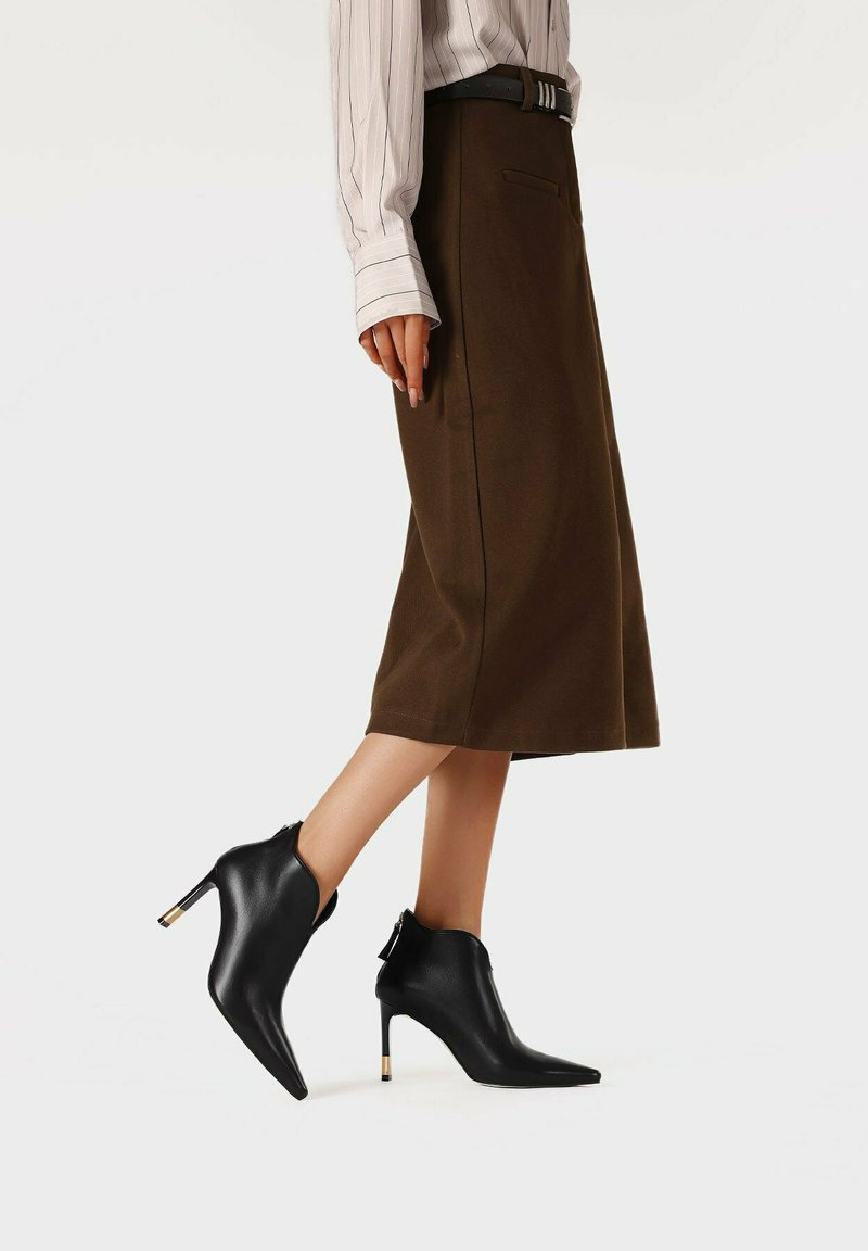 Stivaletti neri alla caviglia con punta affusolata, tacco sottile e dettagli dorati. Realizzati in pelle liscia, presentano un design elegante e moderno.