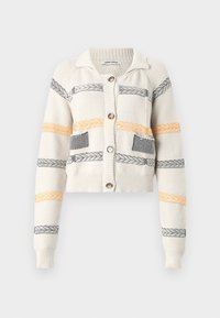 Skraćeni pleteni kardigan u krem boji, s horizontalnim prugama u crnoj i narančastoj boji. Istaknuti detalji uključuju ovratnik i kopčanje na dugmad.