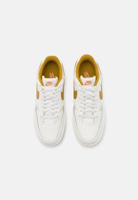 Baskets en cuir blanc avec des accents orange, dotées d'une doublure en maille texturée et d'une fermeture classique à lacets. Logo Nike en orange contrastant.