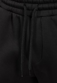 Zwarte joggingbroek met een trekkoord in de taille, zachte stof, geribbelde uiteinden en zijzakken. De textuur is glad met een minimale glans.