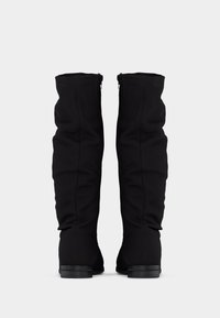 Bottes noires montantes jusqu'au genou avec finition en tissu doux, présentant une coupe ajustée et un design supérieur incurvé. Semelle plate et solide. Détail de fermeture éclair discret.