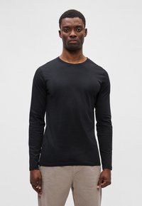 Juodas ilgomis rankovėmis marškinėlis su apvaliu iškirpimu, pagamintas iš lygaus audinio. Aptempta forma su minimaliomis siūlėmis ir be raštų.