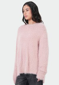 Lichtroze fuzzy trui met een zachte textuur, losse pasvorm, lange mouwen en een ronde hals. Handmatig passende ontwerp en ribbels aan de manchetten.