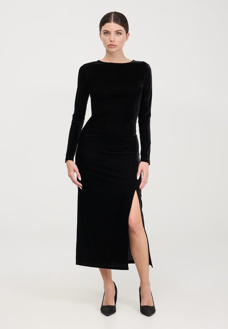 Abito lungo in velluto nero con maniche lunghe, silhouette aderente e spacco fino alla coscia, caratterizzato da un collo rotondo e una texture liscia.