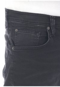 Jeans de denim negro con un diseño clásico de cinco bolsillos, ligeros desgastes y herrajes plateados en los bolsillos delanteros y la cinta de la cintura.