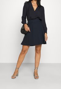 Mörkblå knappad kjol, långärmad topp med v-ringning, zebramönstrade klacksandaler och en liten svart axelväska. Slät tygkvalitet och figursydd design.