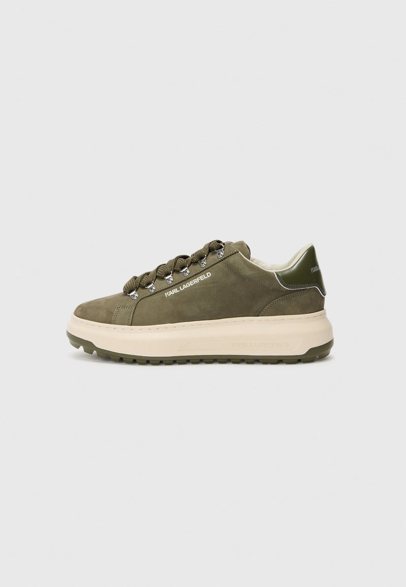 Olive green suede sneaker with thick beige sole, silver-tone hardware, and laces. Features a logo on the side and a textured heel accent.