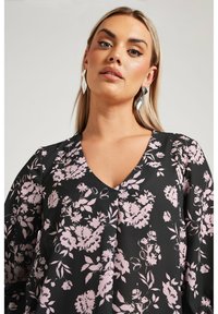 Svart blommig blus med rosa mönster, V-ringad design och lös passform. Har långa ärmar och en mjuk, lätt textur.