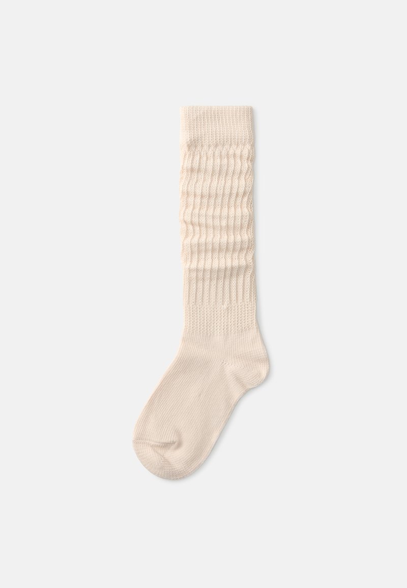 Cremefarvet sok med ribbet tekstur, der har et vaffelmønstret design øverst og en glat nederste del.