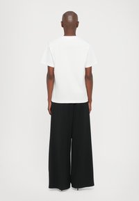 White short-sleeve t-shirt paired with wide-leg black trousers, featuring a smooth texture and minimalist design. No visible branding.
