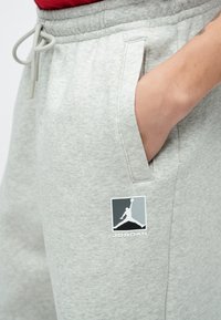 Hellgraue Jogginghosen aus weichem Material, mit einer Seitentasche und einem Jordan-Logo-Patch in Schwarz und Weiß am Bein.