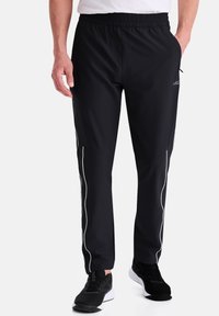 Schwarze Sportpants mit einem elastischen Bund, seitlichen Taschen und weißen Paspeln entlang der Beine, hergestellt aus einem glatten, leichten Material.