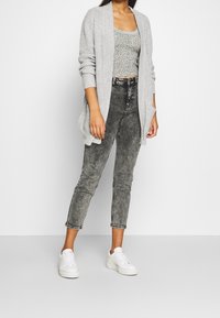 Szary dzianinowy kardigan nałożony na zielony kwiatowy crop top, w zestawieniu z czarnymi spodniami typu high-waisted i białymi sneakerami. Casualowy fason i swobodny design.