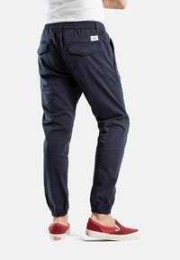 Joggers de algodón en color marino con cinturilla y puños elásticos, que cuentan con dos bolsillos traseros y una pequeña etiqueta de marca en la parte trasera. Combinados con zapatos rojos sin cordones.