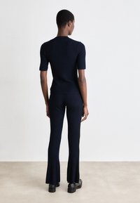 Set composto da top a coste navy e pantaloni a palazzo. Maniche corte e silhouette aderente, con una texture morbida e una leggera elasticità. Scarpe basse visibili.