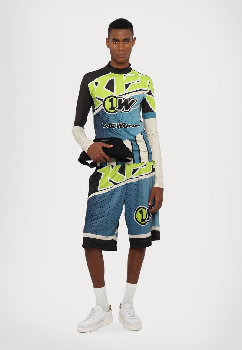 Multicolored athletic outfit featuring a long-sleeve top with green and black geometric patterns and blue shorts with logos and accents.