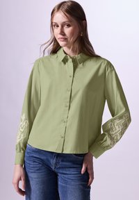 Camicia button-up verde chiaro con maniche lunghe, caratterizzata da dettagli ricamati in beige chiaro sui polsini. Vestibilità casual con una texture morbida.