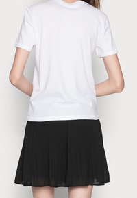 Vit t-shirt med kort ärm och rund halsringning, matchad med en svart plisserad kjol som slutar ovanför knäna. Tillverkad av mjukt bomullsmaterial.