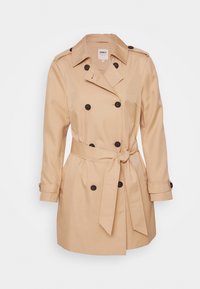 Beżowy dwurzędowy płaszcz trench w gładkiej tkaninie. Posiada pasek w talii, duże brązowe guziki oraz długie rękawy z zapięciem na guziki.