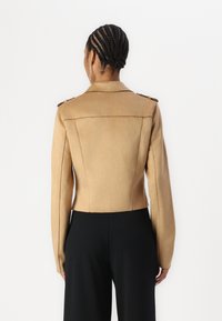 Béžová faux suede zkrácená bunda se strukturovaným střihem, ramenními epauletami, dlouhými rukávy a vertikálními švy. Zobrazená zpětná strana.
