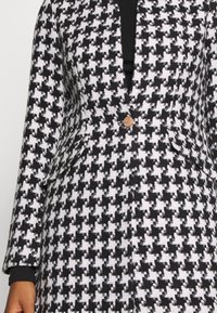 Blazer à motif pied-de-poule noir et blanc avec un col cranté, une fermeture à un bouton et deux poches avant. Tissu texturé.