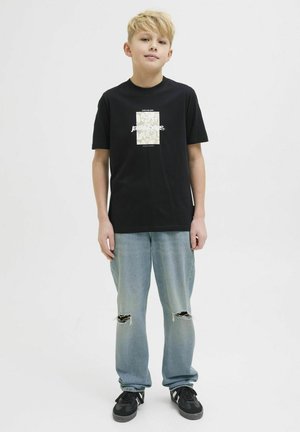 T-shirt noir à col rond avec un motif léger sur la poitrine, associé à un jean bleu clair déchiré et des baskets noires.