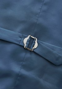 Sininen kangas, jossa on sileä pinta, sisältää metallisen soljen kiinnityksenä, mikä korostaa siistiä, minimalistista muotoilua.