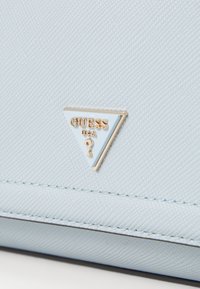 Light blue textured handbag featuring a triangular gold-accented logo. Smooth surface with detailed stitching around edges.