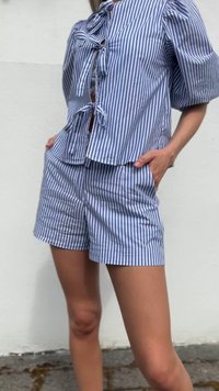 Randig blå och vit skjorta med puffärmar och knytband fram, kombinerad med matchande shorts med fickor och veck.
