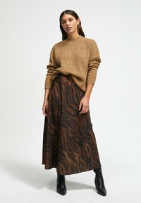 Pull en tricot marron avec un motif texturé, associé à une jupe maxi à imprimé animal marron et noir. Le modèle porte des bottes noires à la cheville.