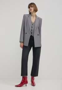 Blazer grigio doppiopetto con rever a punta, indossato sopra un gilet grigio con bottoni; abbinato a jeans neri a gamba dritta e stivaletti rossi lucidi.