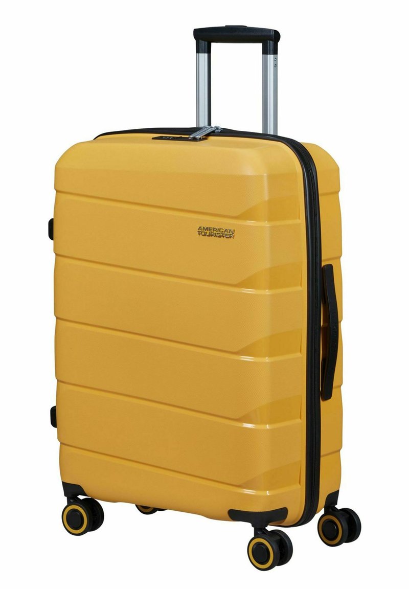 Hard-shell gele koffer met gestructureerde strepen, zwarte rits en handgreep, uitschuifbare aluminium handgreep en vier wielen met gele accenten.