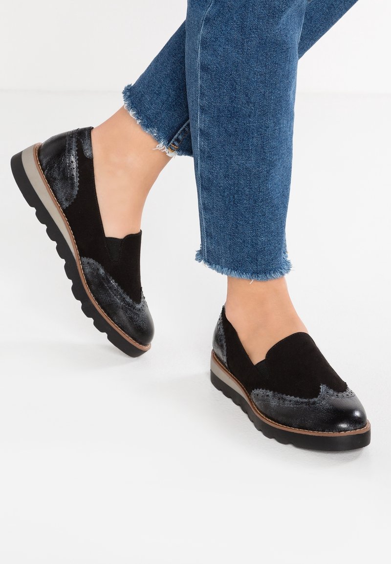 Chaussures noir à enfiler combinant des textures brillantes et en suède, avec une semelle rembourrée et des détails de couture subtils.