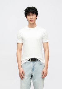 Wit T-shirt met korte mouwen, gemaakt van katoen, gecombineerd met lichtblauwe denim jeans. Heeft een klassieke ronde halslijn en een zwarte riem.