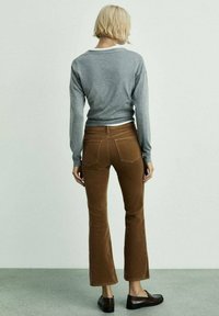 Gray long-sleeve sweater, brown flared corduroy pants, and dark brown loafers. The outfit features a snug fit with a minimalist design.