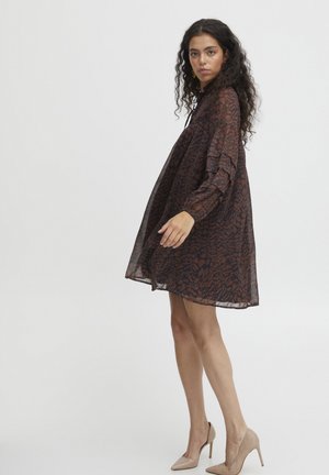 Braunes, durchscheinendes Kleid mit einem strukturierten Blumenmuster, langen Ärmeln und einer fließenden Silhouette. Kombiniert mit nude-farbigen High-Heels.