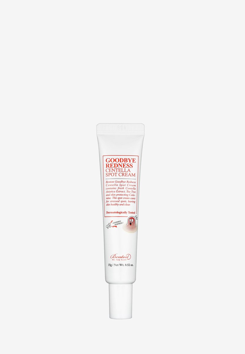 Tubo de plástico blanco con tapa de flip-top, etiquetado "Crema para manchas Centella Goodbye Redness" en rojo, con un ícono de fantasma de dibujos animados y detalles botánicos.
