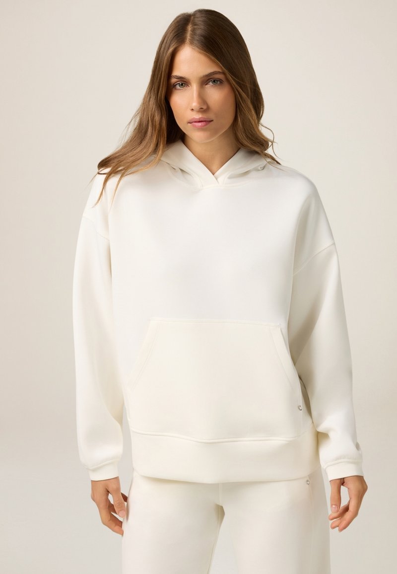 Sudadera blanca con capucha, con un bolsillo frontal, corte relajado y puños acanalados. Textura suave y diseño minimalista con un sutil detalle de marca.