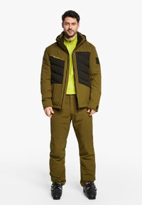 Skijacke in Olivgrün mit schwarzen gepolsterten Vorderteilen, kombiniert mit passenden Hosen. Mit einem Reißverschluss vorne und einer Kapuze. Schwarze Skistiefel sind enthalten.