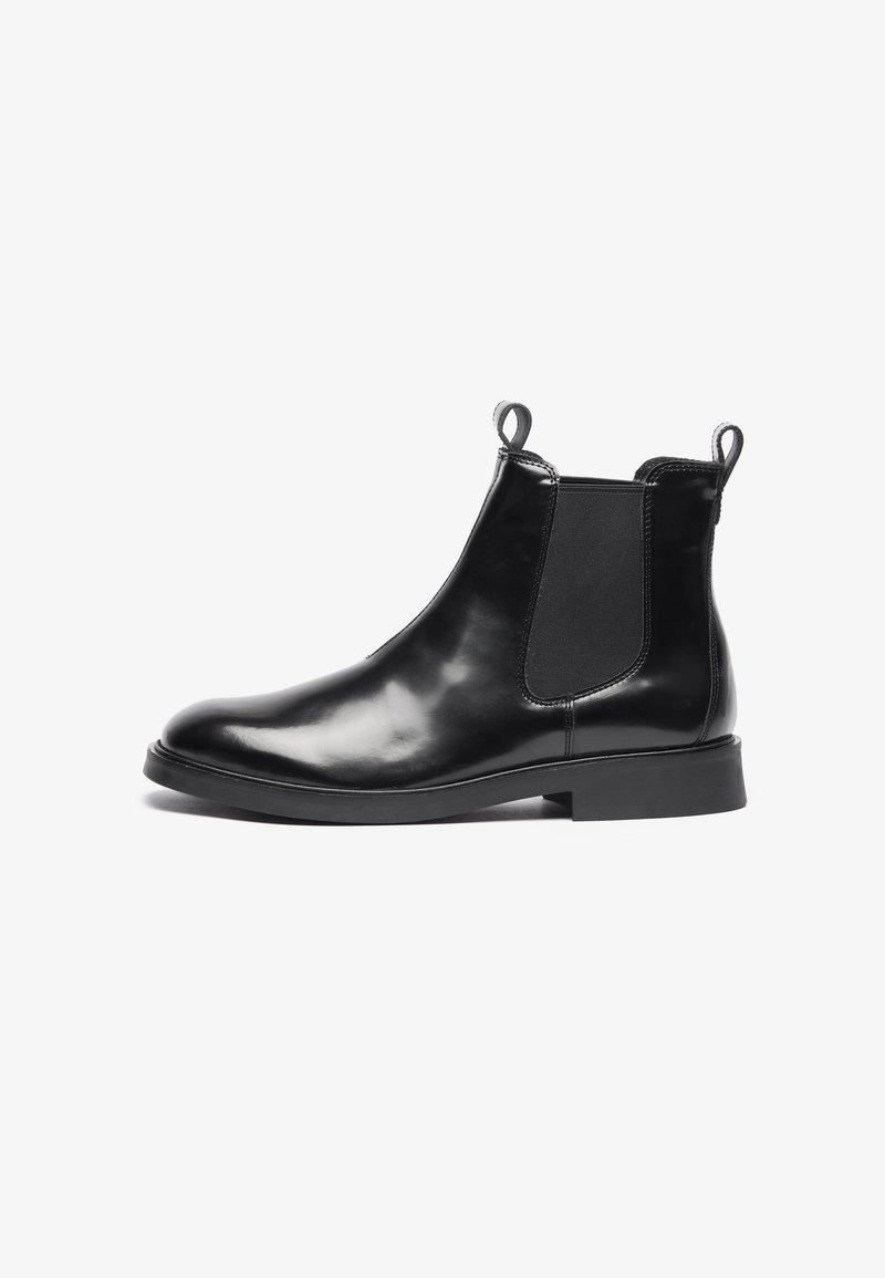 Botte Chelsea en cuir noir avec panneaux latéraux élastiques, languettes à la cheville, talon bas et bout arrondi lisse.